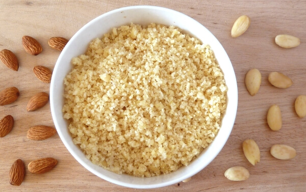 Coursely ground almond flour in a bowl surrounded by whole almonds