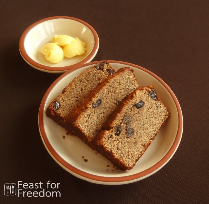 Slices of banana bread with raisins on a plate, with a small dish of butter next to it