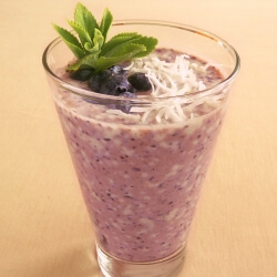 Fresh blueberry and coconut smoothie in a glass garnished with blueberries, shredded coconut and fresh stevia leaves