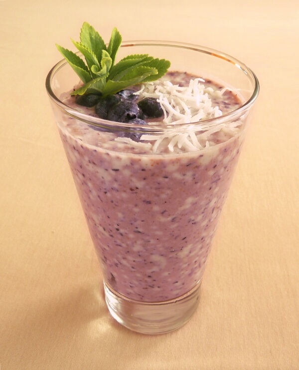 Fresh blueberry and coconut smoothie in a glass garnished with blueberries, shredded coconut and fresh stevia leaves