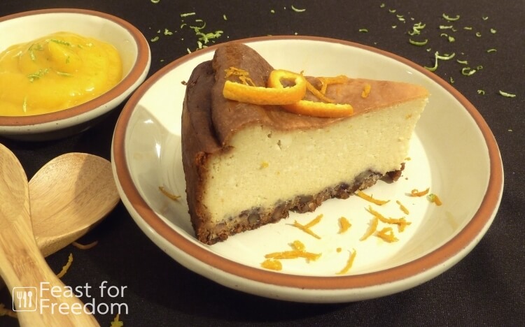 New York style baked cheesecake on a plate, next to a small bowl of Mango Sauce, sprinkled with orange and lime zest