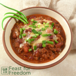 Bowl of chili con carne sprinkled with grated mozzarella and sliced green onions