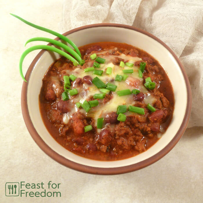 Bowl of chili con carne sprinkled with grated mozzarella and sliced green onions