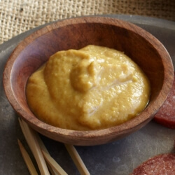 Dijon mustard in a small wooden bowl on a platter with sausage medallions