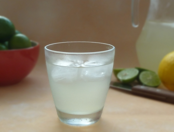 Lemonade in a glass next to lemons and limes