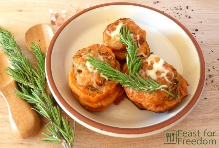 Sweet potato stackers on a plate sprinkled with Parmesan cheese and a sprig of fresh rosemary